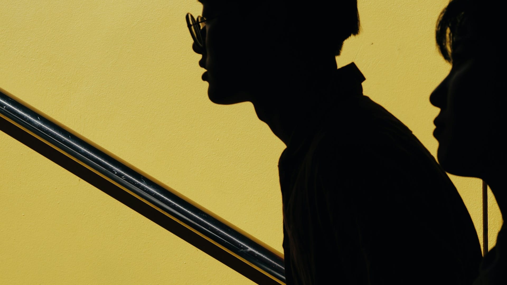 Two human profile silhouettes side by side against a yellow wall