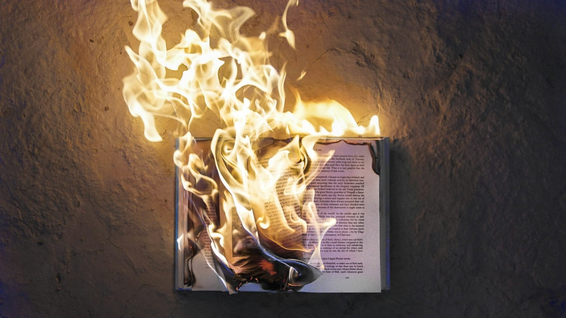 Open book burning with bright flames against a stone wall