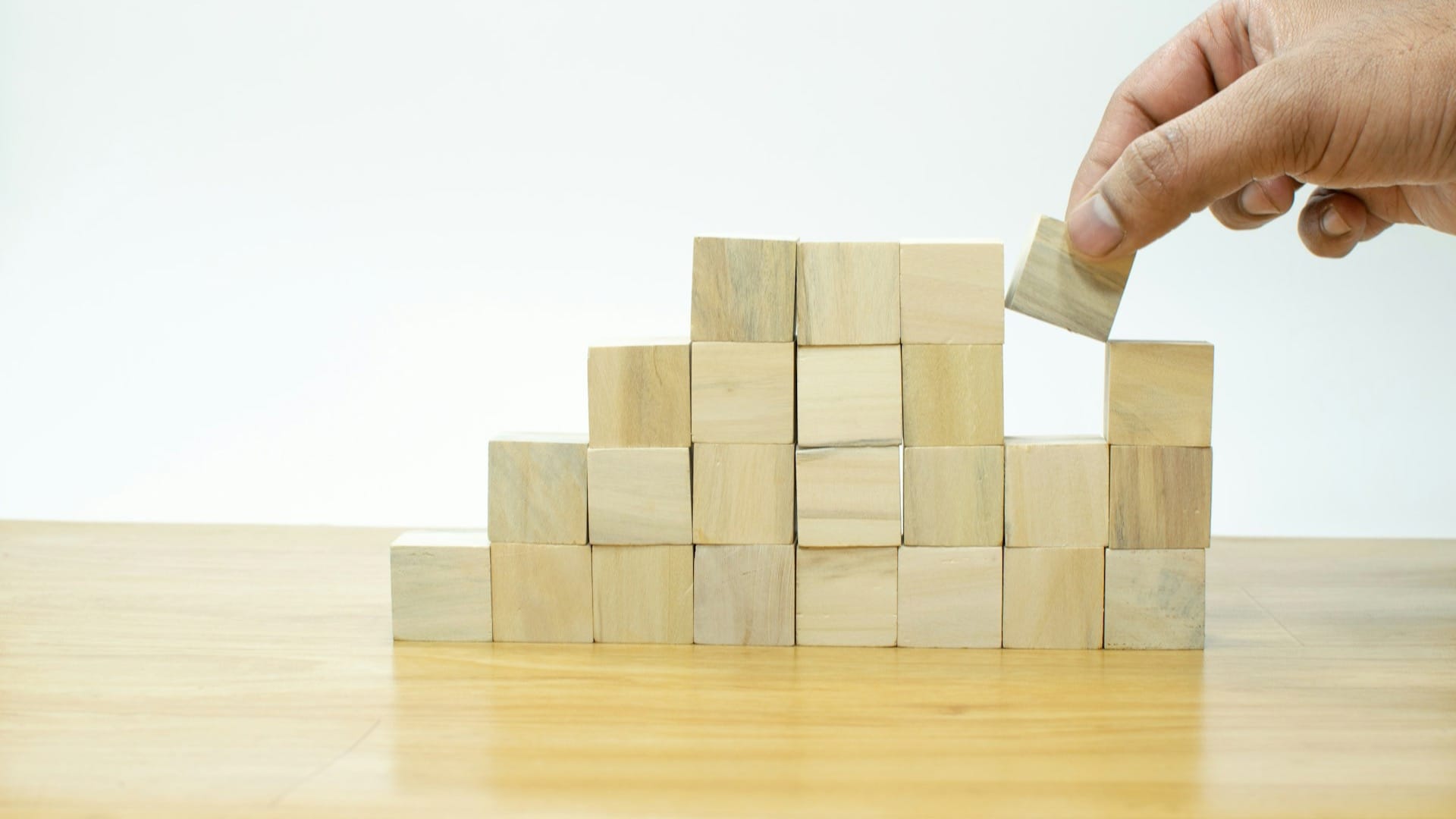 A hand stacking a wooden block onto a growing pile of blocks