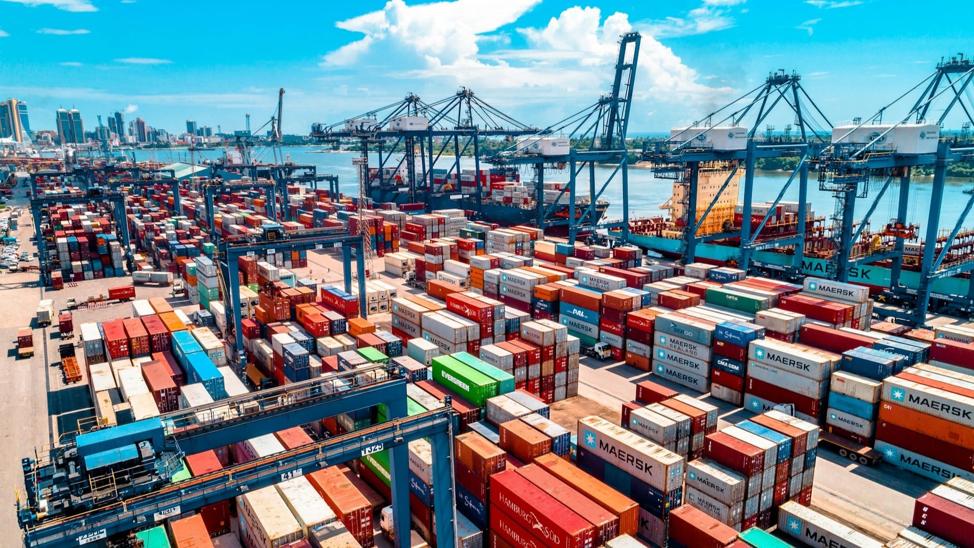Stacked shipping containers at a busy port, waiting to be moved