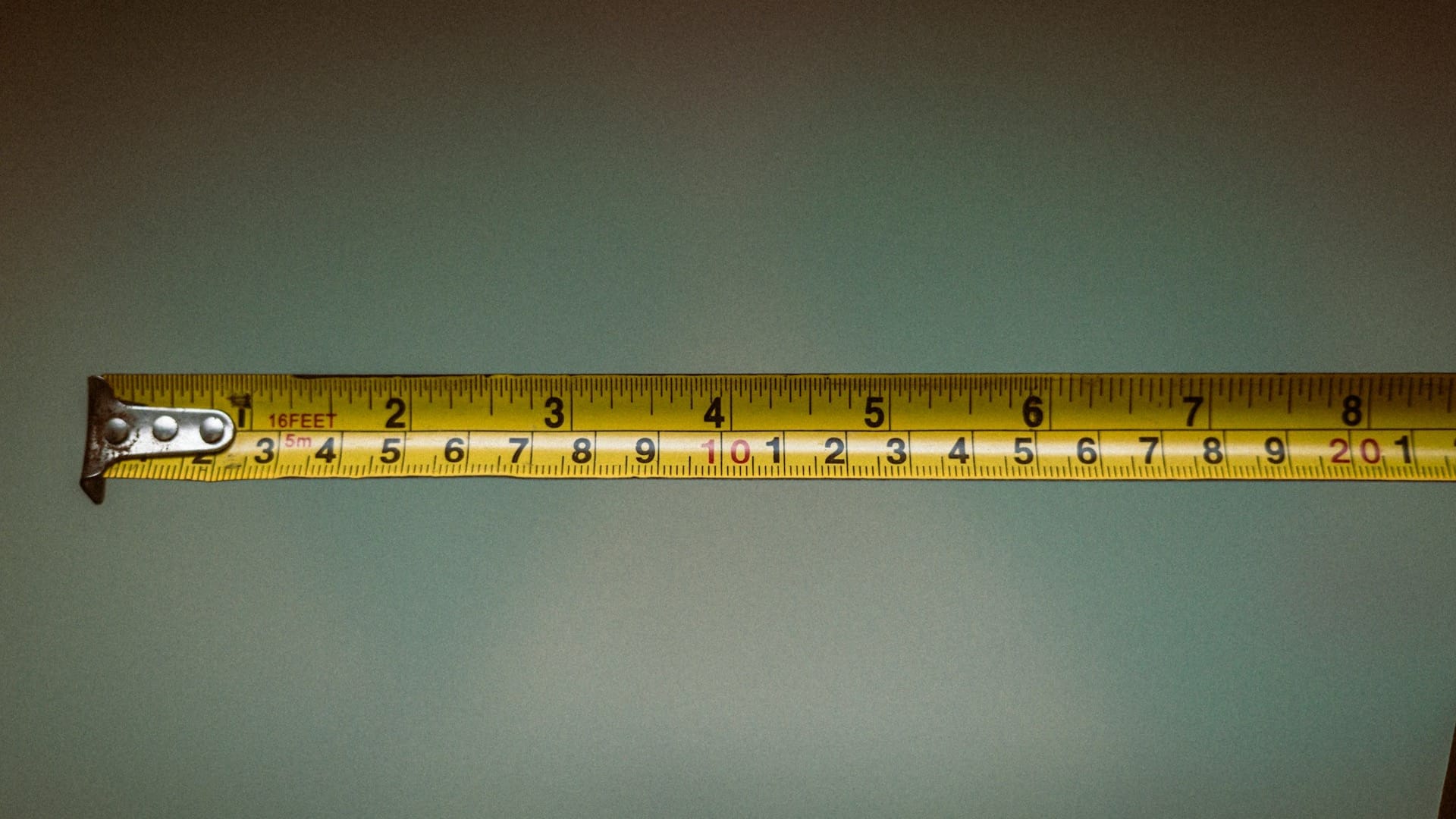 A hand holding an extended tape measure against a plain grey background