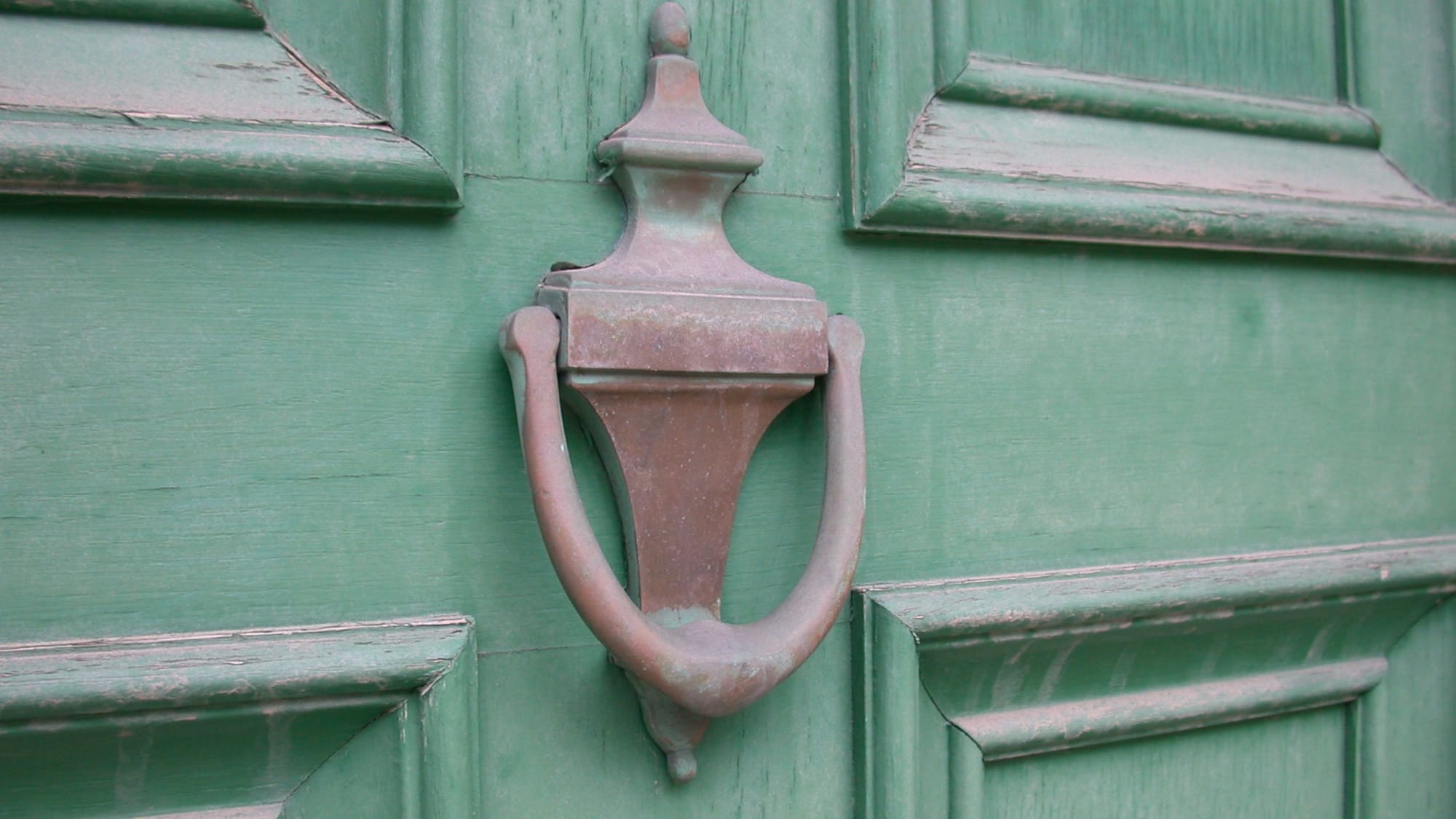 A weathered brass door knocker on a green painted wooden door.