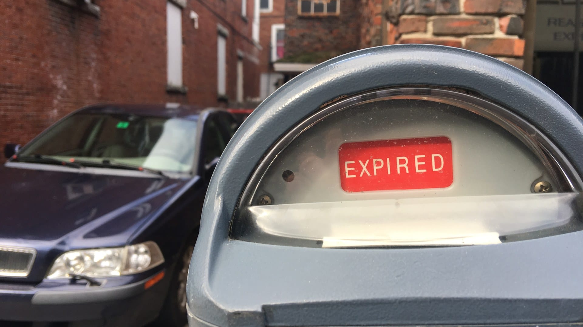 A parking meter showing a red EXPIRED flag, with a parked car behind it.