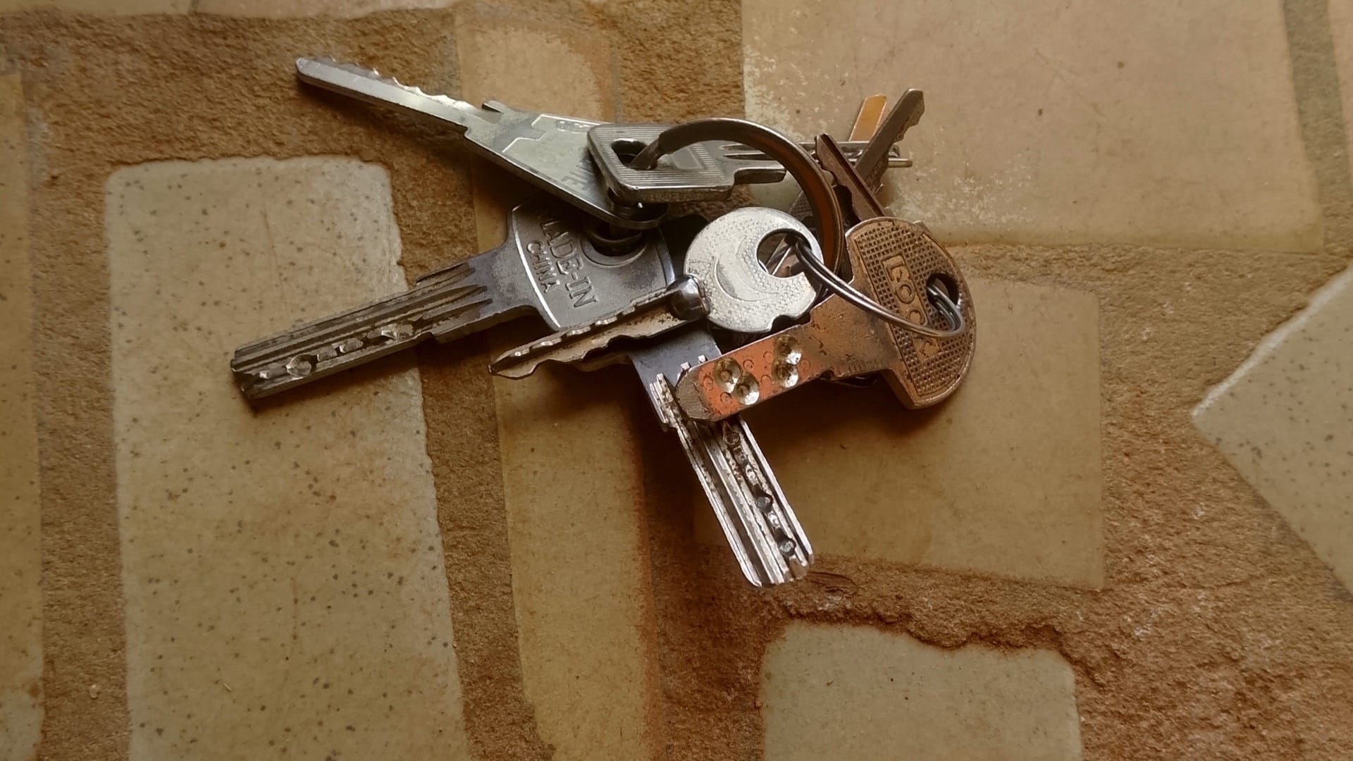 Six different metal keys share one ring on a patterned stone floor.