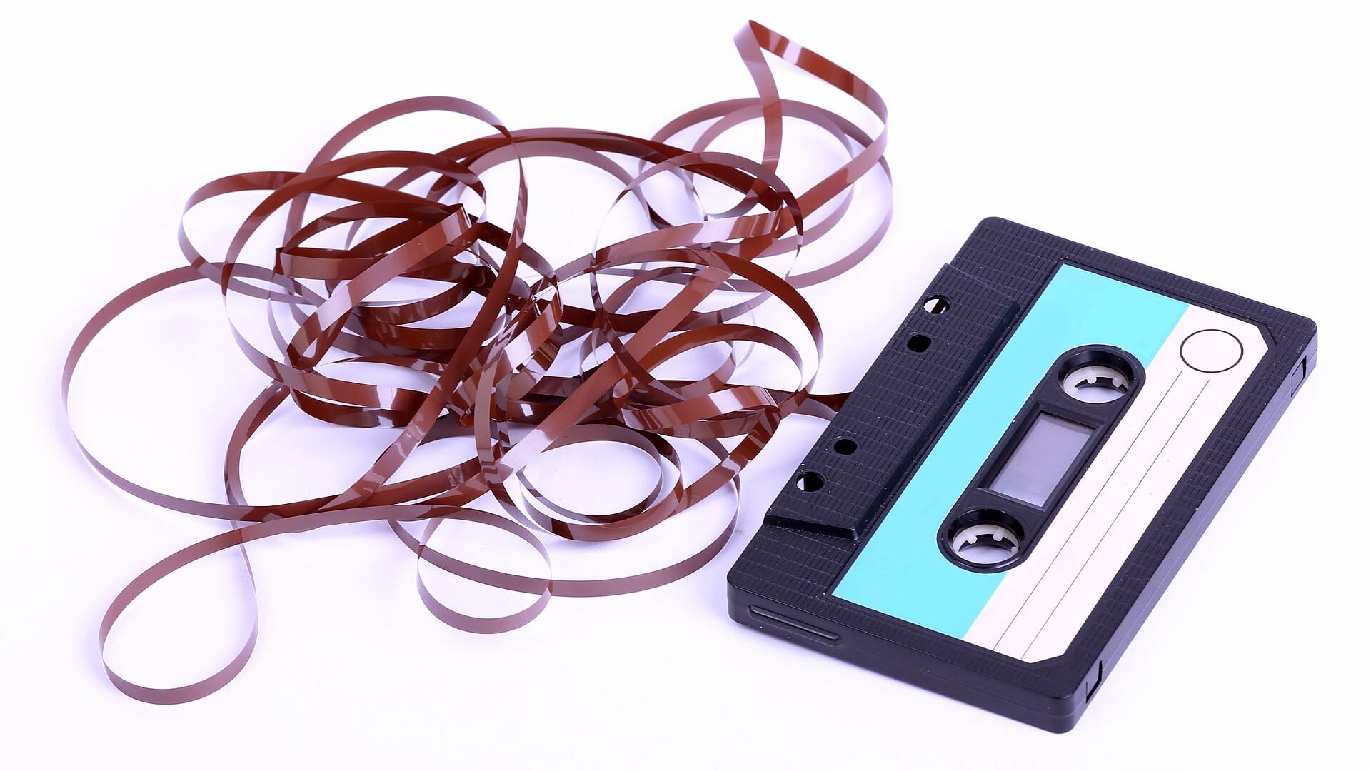 A black compact cassette on a white surface with its brown tape unspooled beside it.