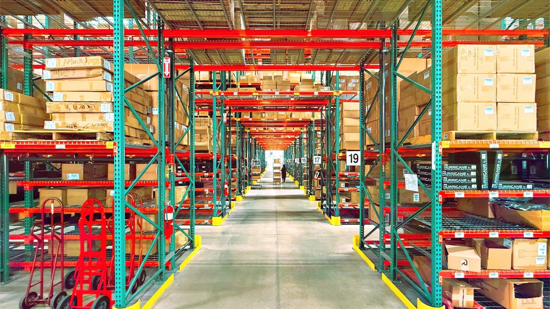 Cardboard boxes fill red and green warehouse racks along a central aisle.