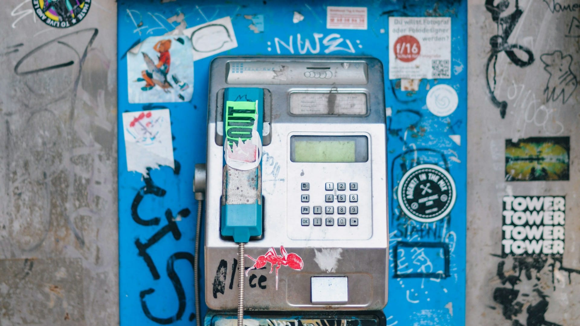 A turquoise public telephone surrounded by stickers and graffiti in Berlin.