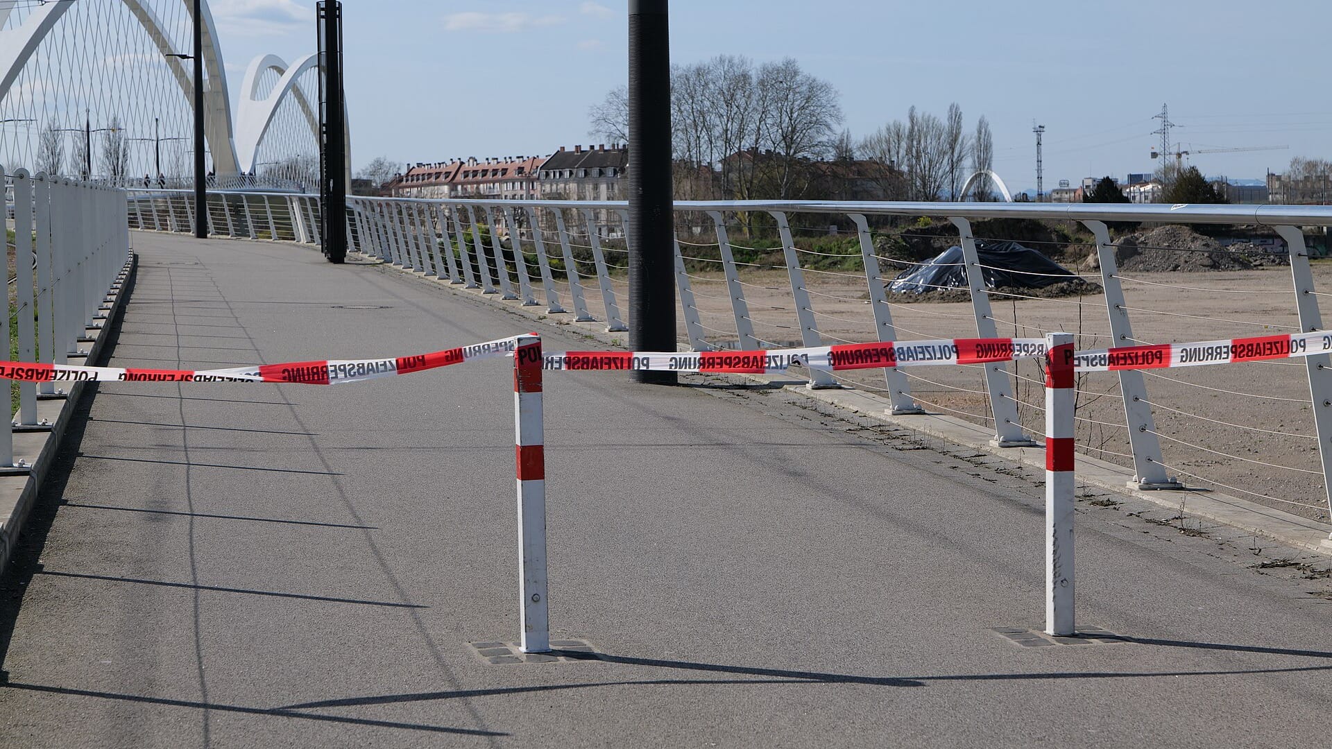 Red-and-white police tape stretched between two bollards, closing a footpath on a bridge.