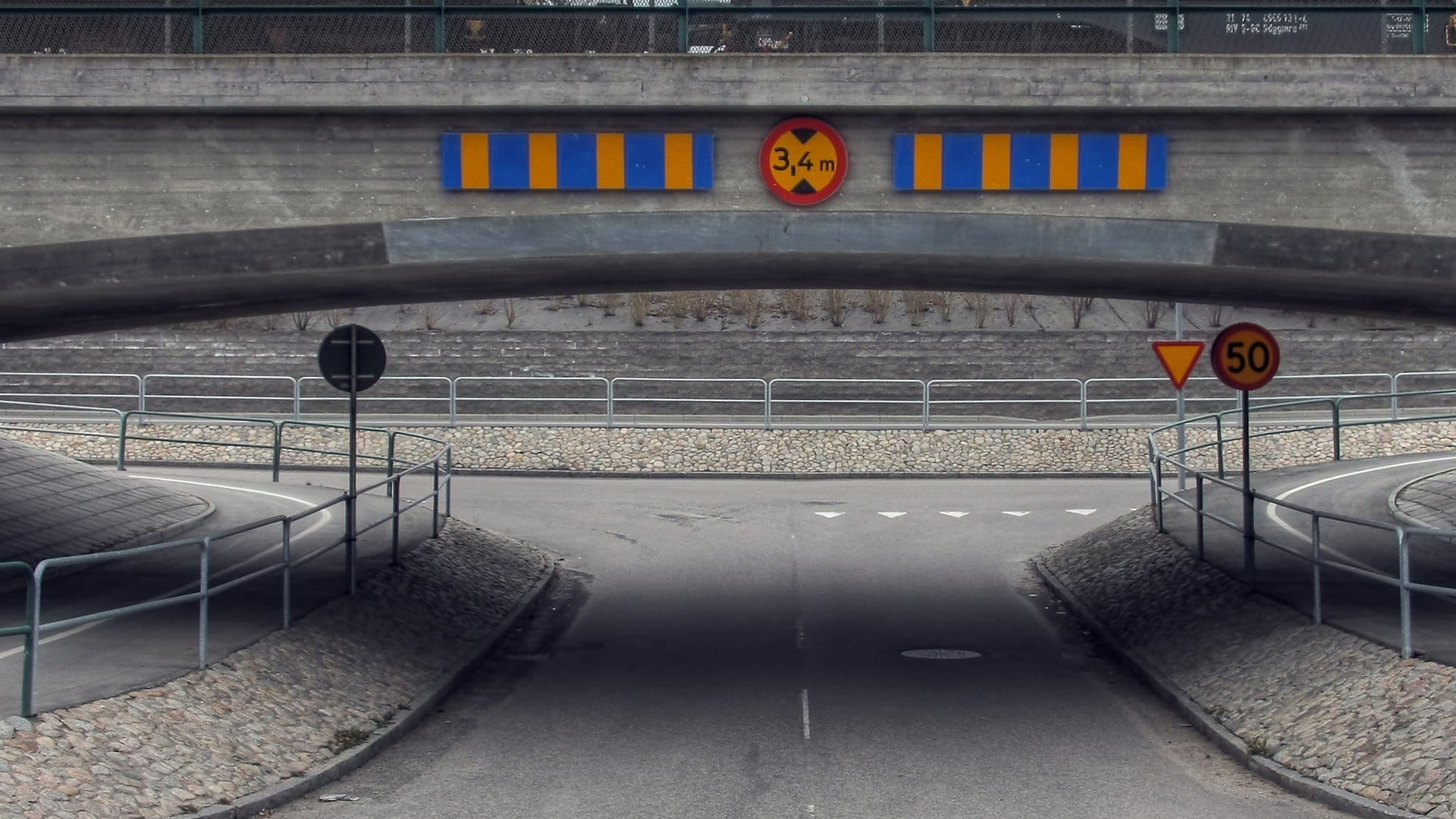 A concrete road underpass with a 3.4 metre height-limit sign and striped warning boards mounted on the bridge above the lane.