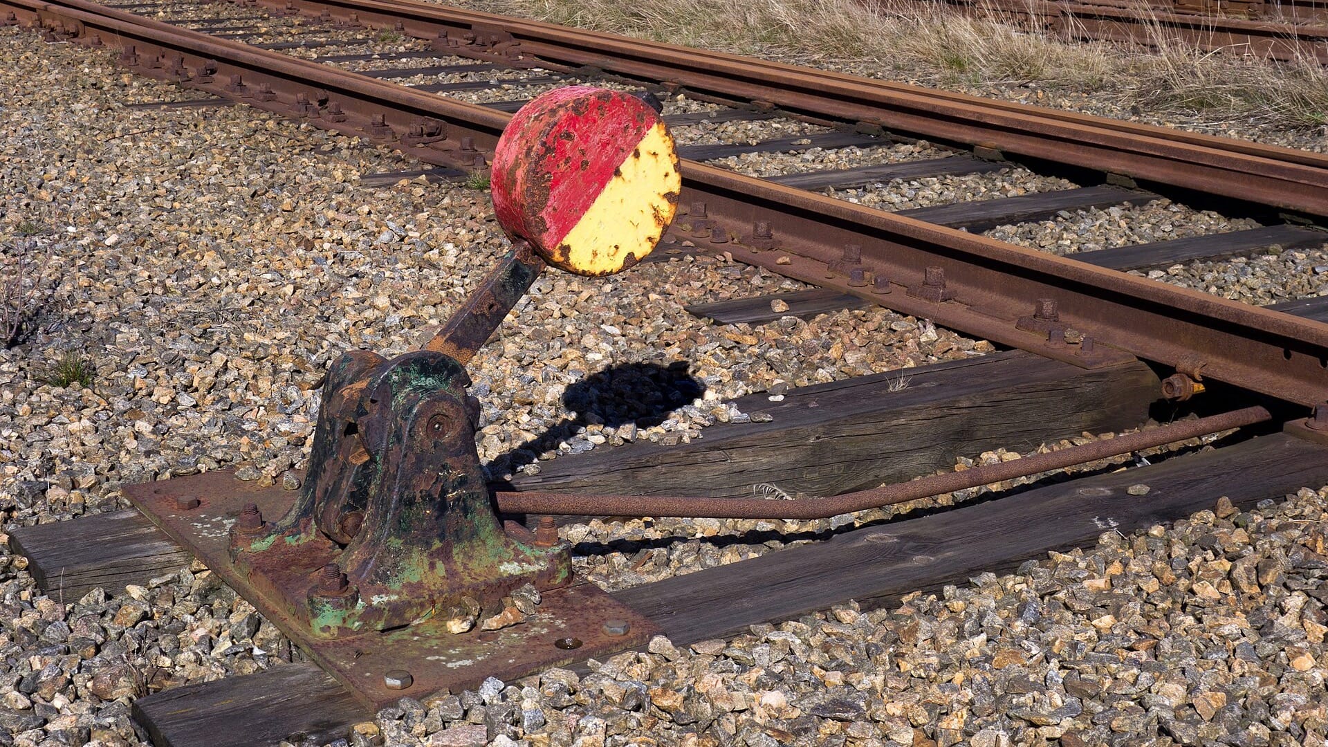 A weathered railway switch lever stands beside tracks that divide in several directions.
