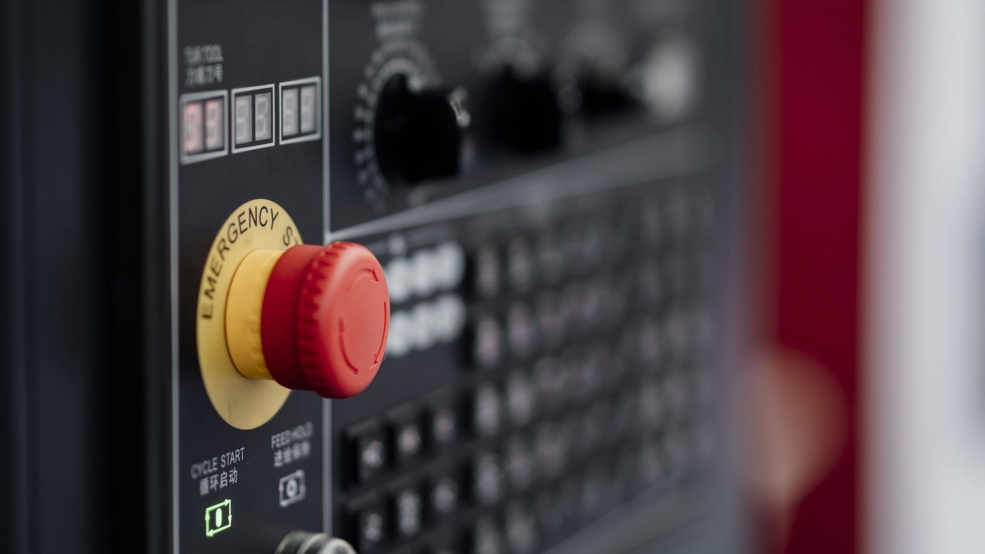 A red mushroom-head emergency stop button on a yellow ring, set into the dark control panel of a factory machine.