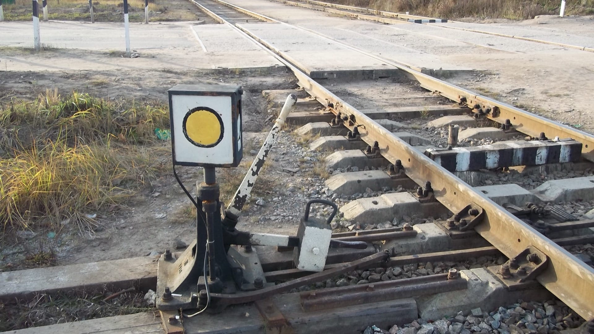 A manual railway switch and yellow signal beside tracks that divide at a level crossing.