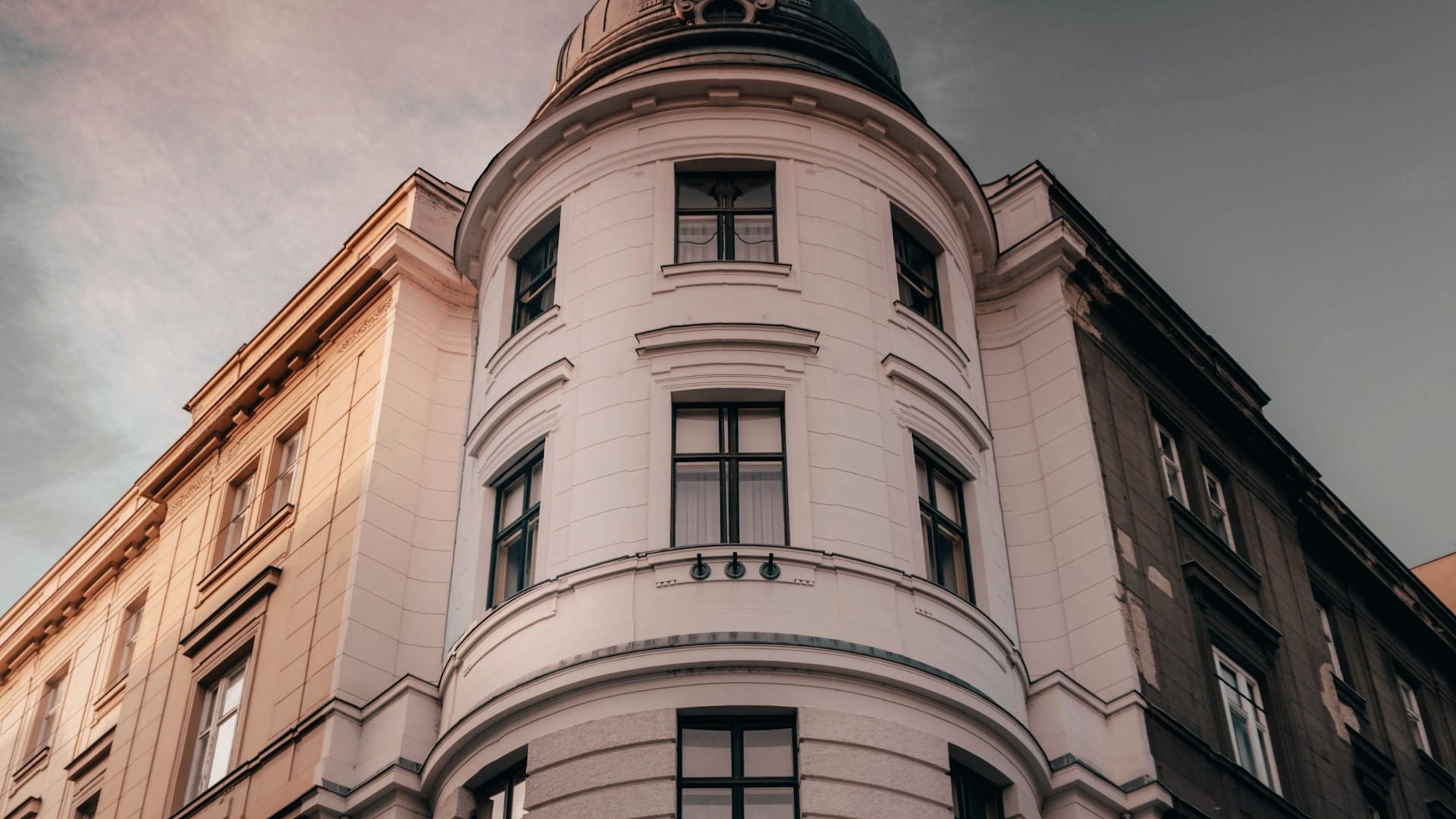 An older corner building with a rounded facade, tall windows, and a domed roof.