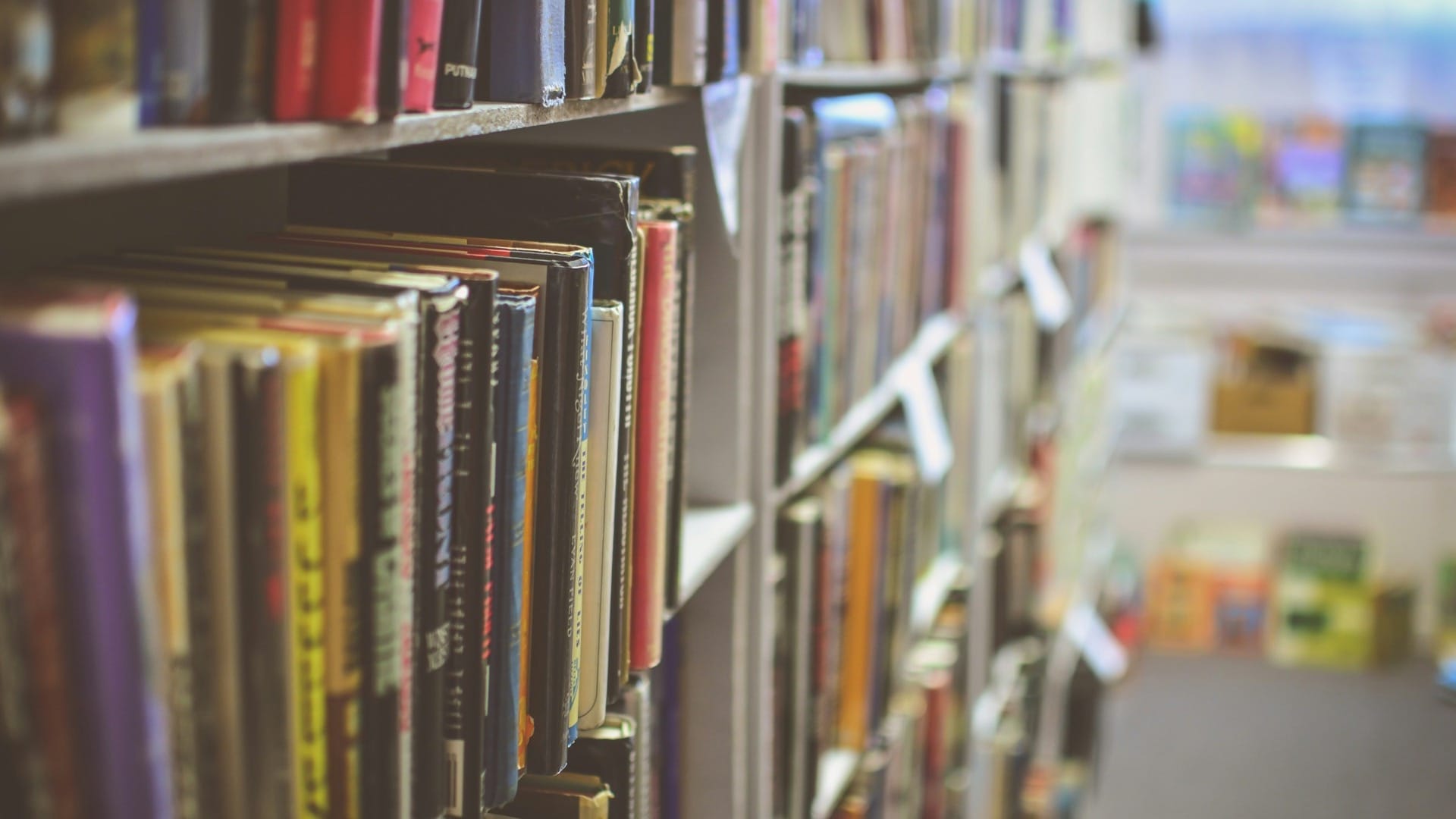 Worn books line wooden shelves, with the library aisle fading out of focus.