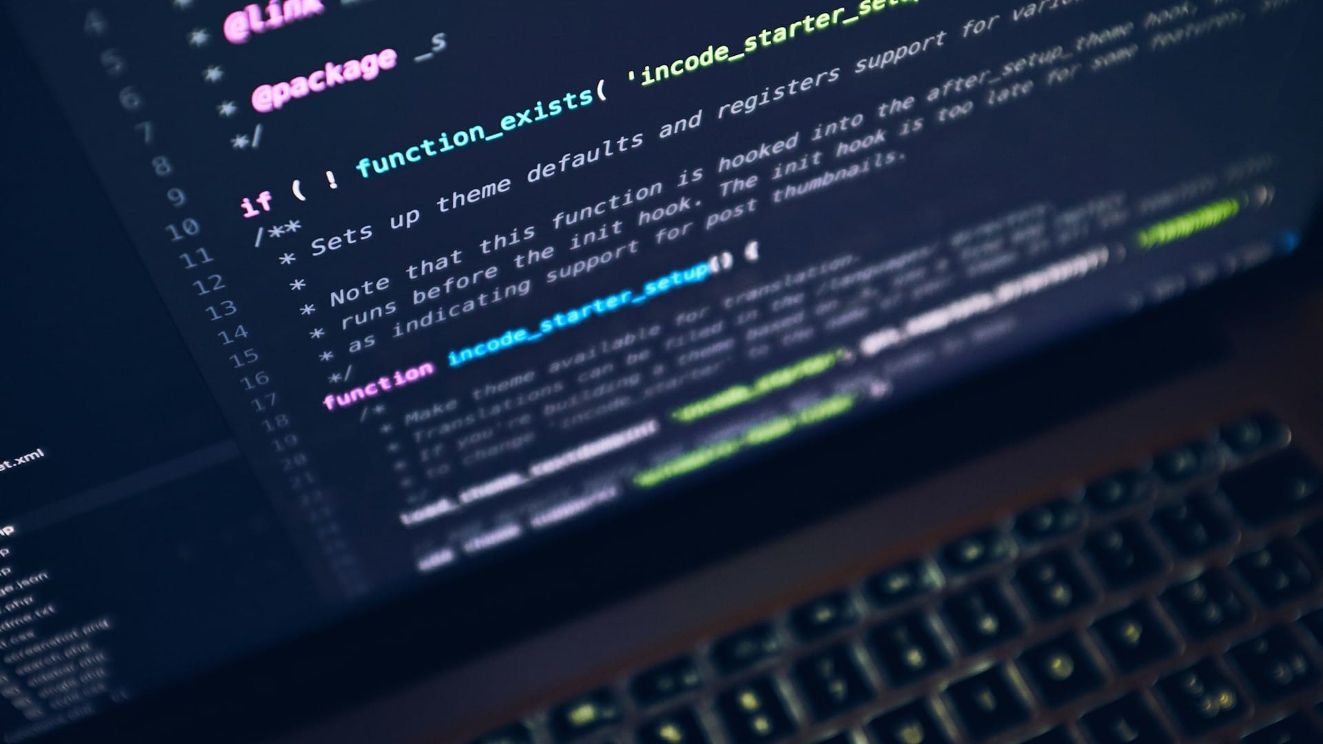 A laptop keyboard beneath a screen displaying source code in a dark editor.