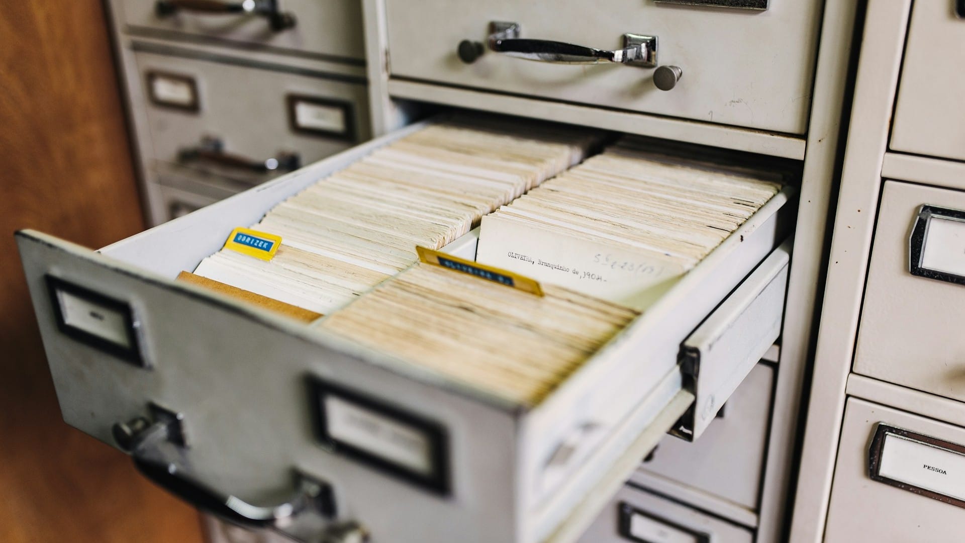 An open metal filing cabinet drawer holds rows of paper index cards.