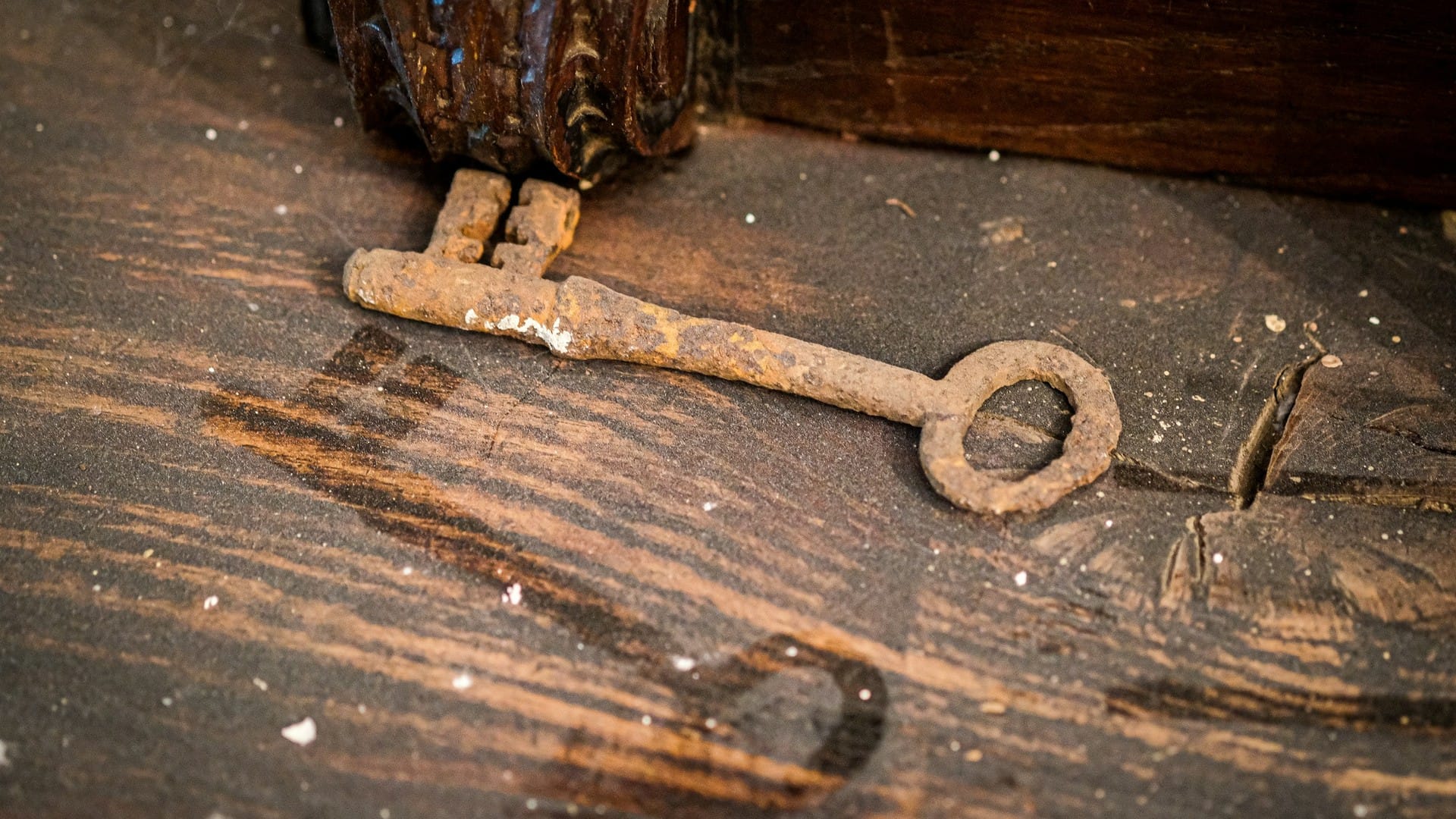 A rusty iron key rests on a worn wooden surface beside an old lock.