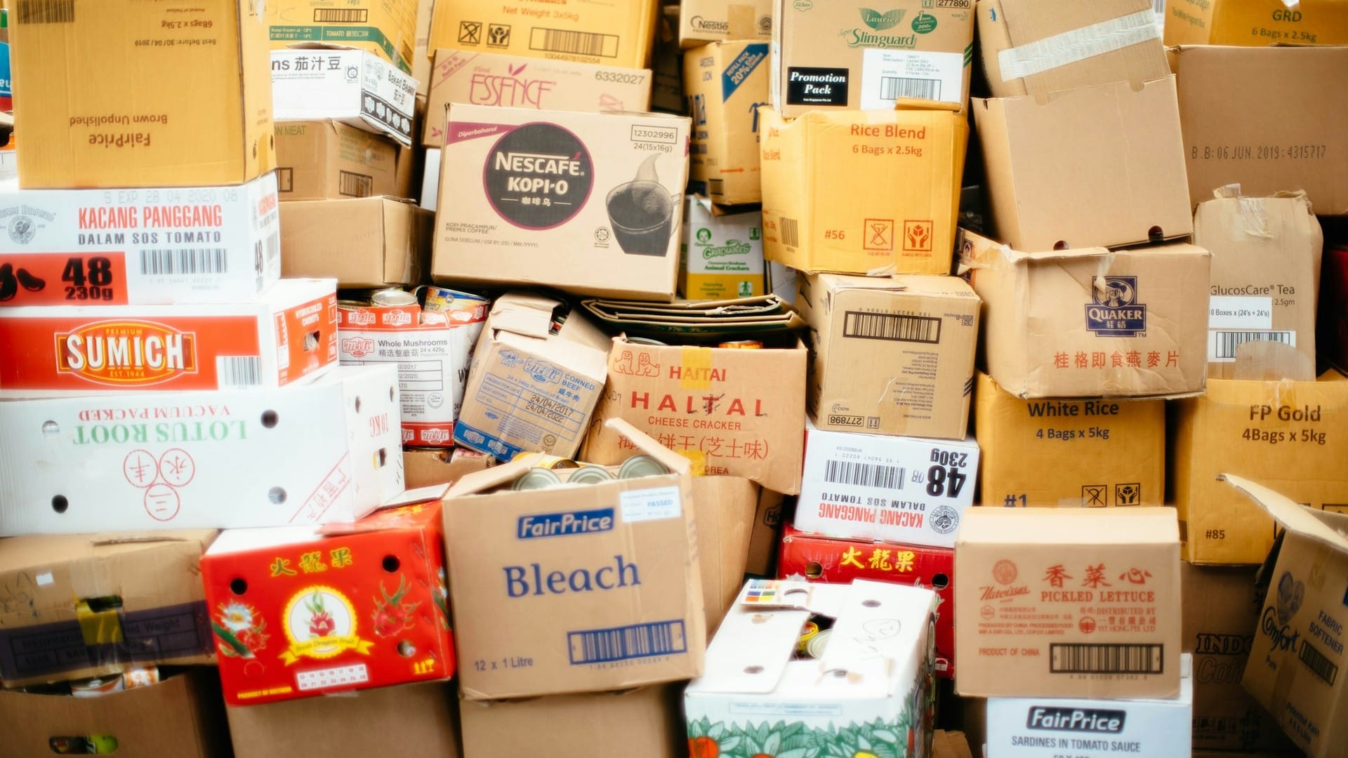Printed cardboard cartons stand in a dense stack awaiting handling.