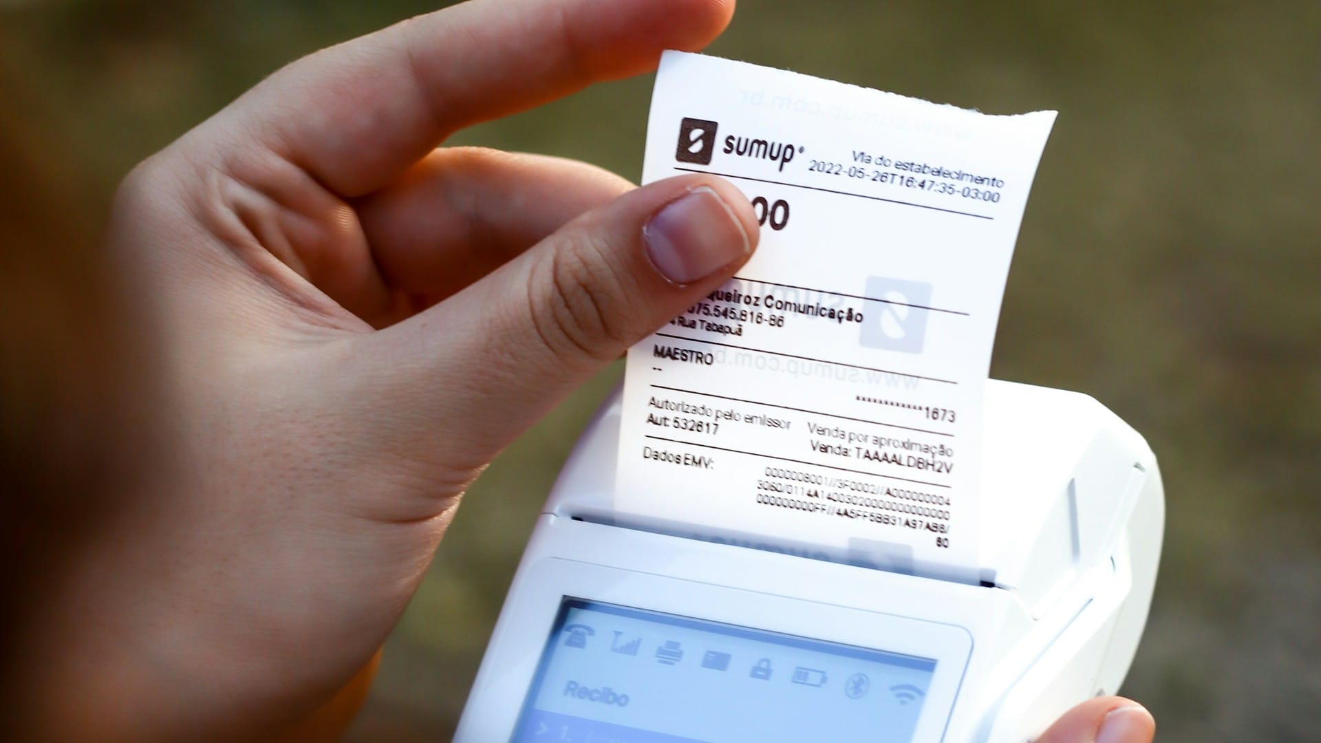 A hand pulls a printed receipt from a white card-payment terminal.